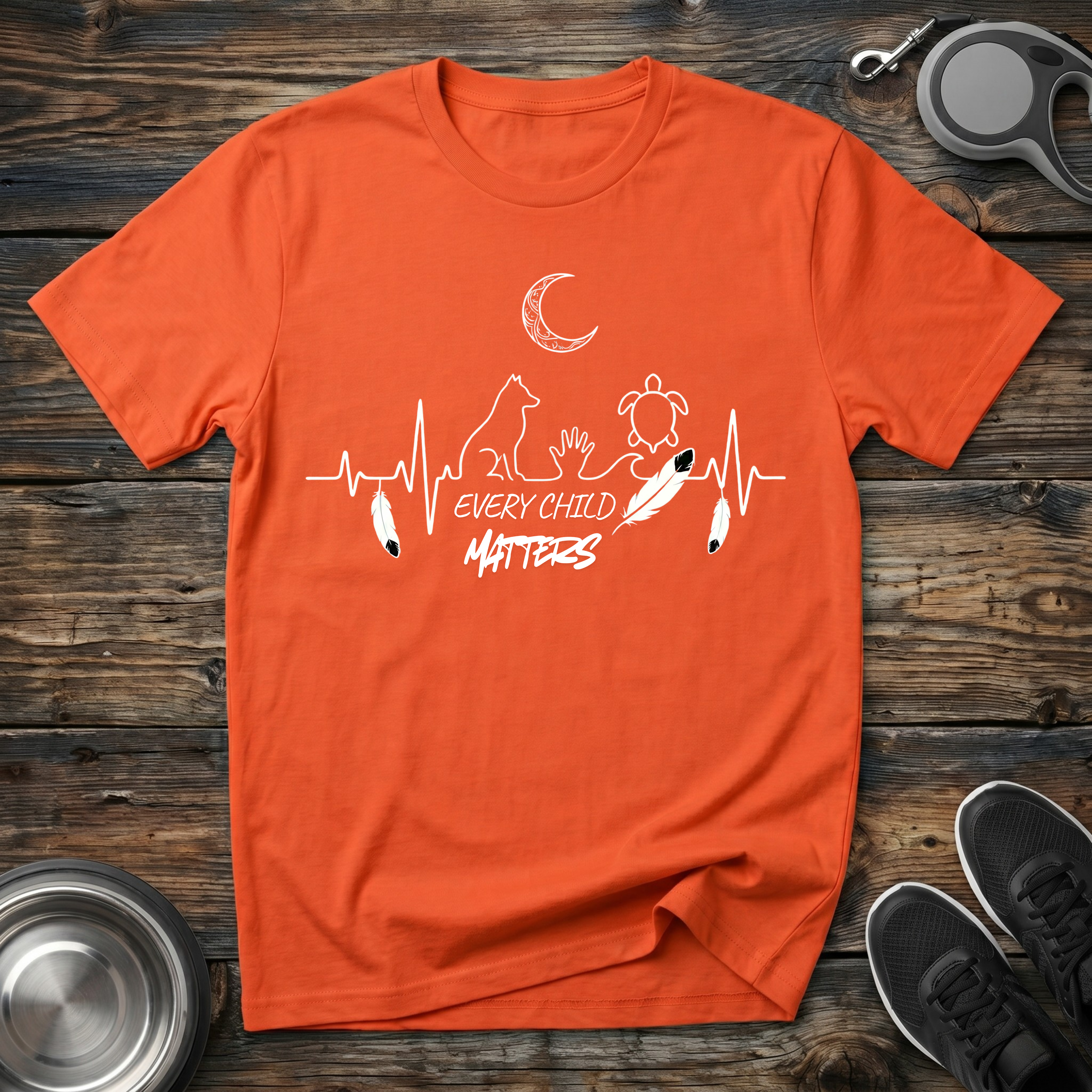 Orange graphic t-shirt with heartbeat line art featuring cat, turtle, moon and Every Child Matters message