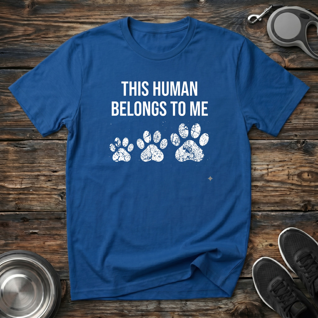 Royal blue unisex t-shirt with bold white "This Human Belongs To Me" lettering and three distressed white paw print graphics — funny dog owner gift tee from the dog's perspective