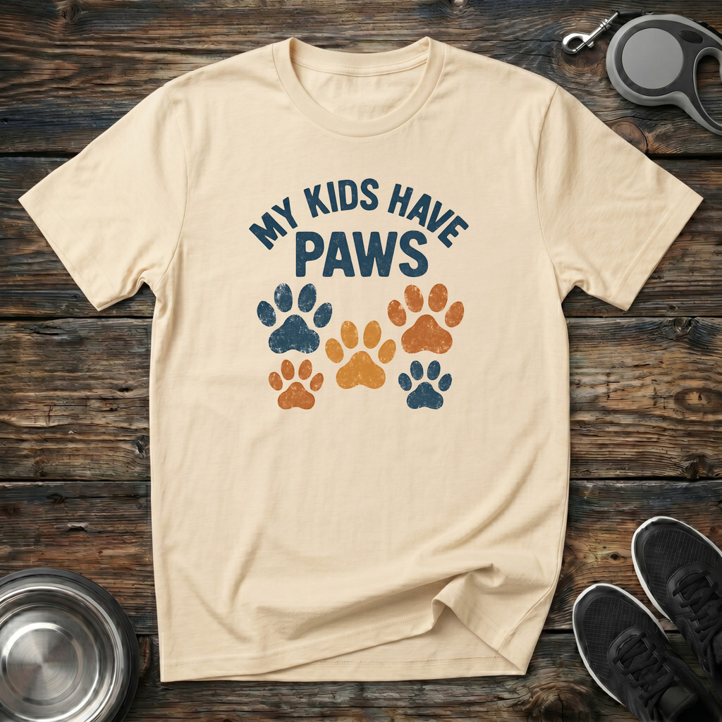 Cream unisex t-shirt with retro arched "My Kids Have Paws" lettering and distressed multicolor navy, orange and gold paw print graphic — funny dog mom and pet parent gift tee