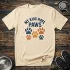 Cream unisex t-shirt with retro arched "My Kids Have Paws" lettering and distressed multicolor navy, orange and gold paw print graphic — funny dog mom and pet parent gift tee