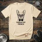 Cream unisex t-shirt with detailed hand-drawn French Bulldog wearing glasses and bow tie graphic and bold "Pardon My French" lettering — funny Frenchie lover gift tee