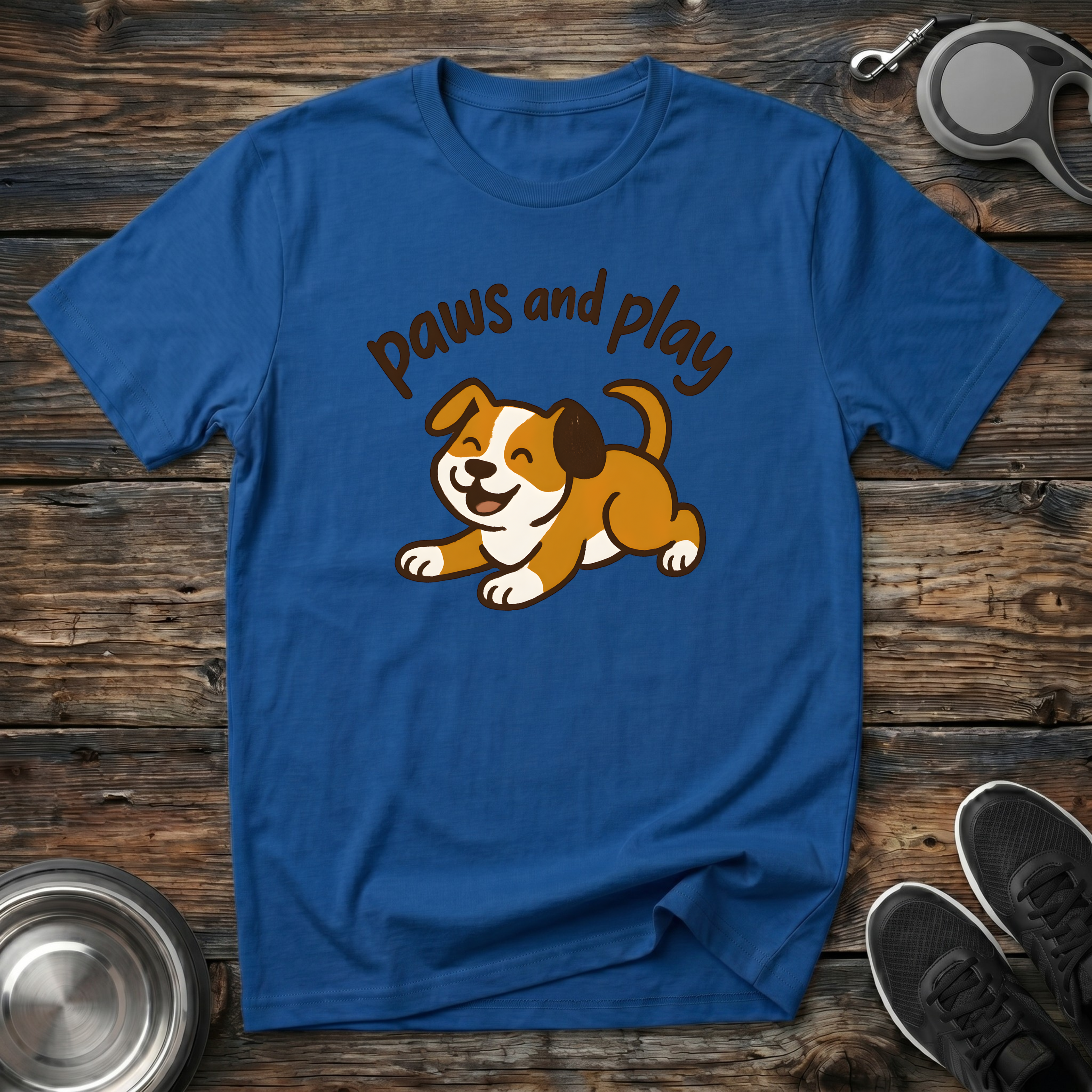 Royal blue unisex t-shirt with kawaii golden brown puppy play-bow illustration and warm brown arched "Paws and Play" script lettering — cute dog lover gift tee for puppy parents and dog moms