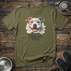 Military green unisex t-shirt with soft watercolor Pitbull portrait in blush pink and grey tones and elegant "Proud Pitbull Mom" dark script lettering — beautiful bully breed lover gift tee