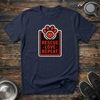 Navy blue unisex t-shirt with bold red white and black badge graphic featuring a paw print with heart center and "Rescue Love Repeat" block lettering — animal rescue advocate dog lover gift tee