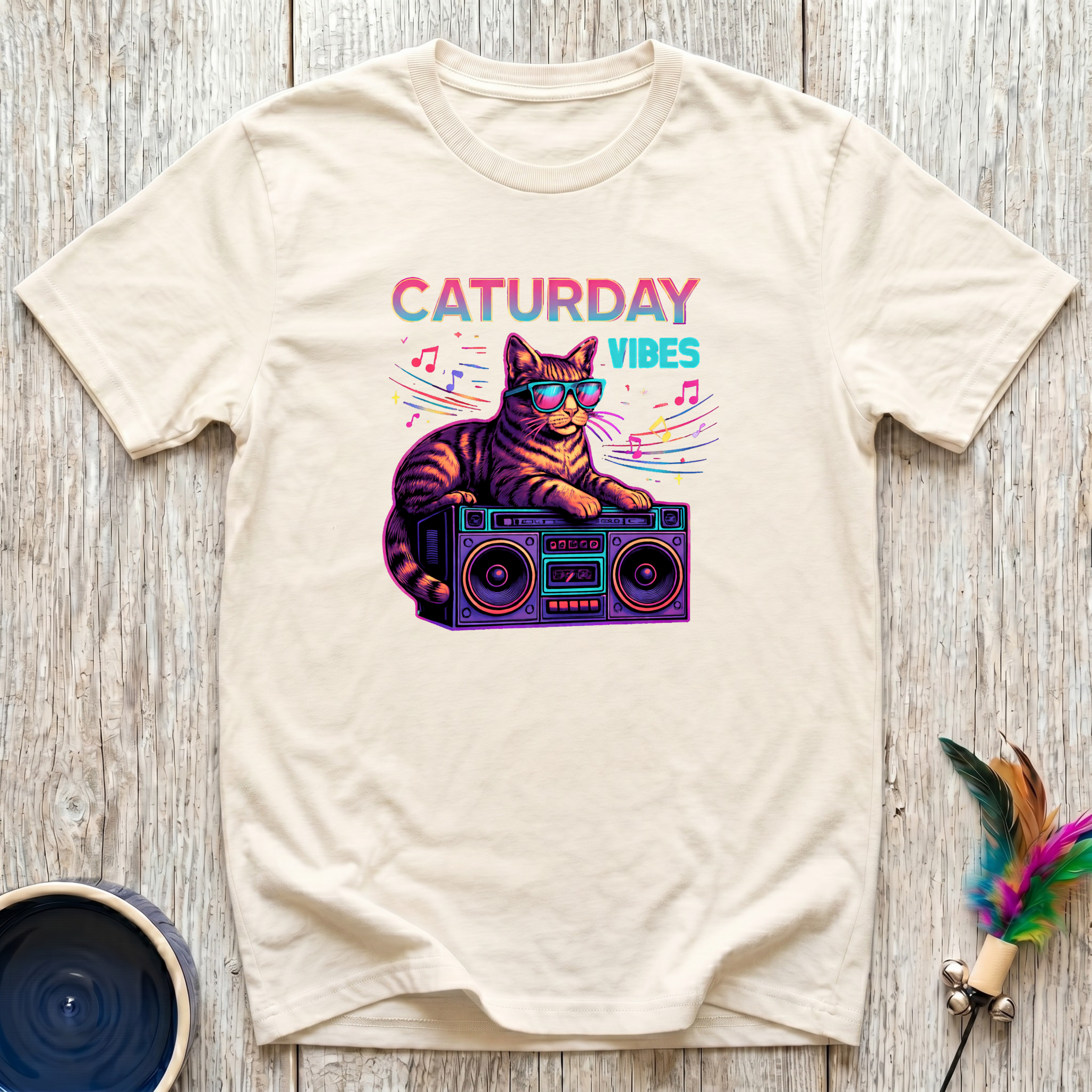 Cream unisex t-shirt with retro tabby cat wearing sunglasses on a boombox graphic and colorful "Caturday Vibes" neon lettering — funny cat lover gift tee